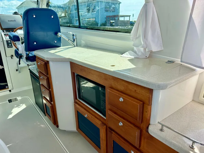 Slide: The Image of 2008 Back Cove 33 Express interior with wooden cabinetry, microwave, and blue captain's chair. - 16