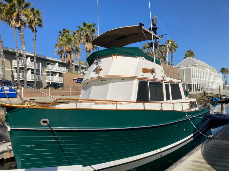 The Image of 1985 Grand Banks 42 Classic yacht docked, featuring green hull and white cabin, with palm trees nearby. - 0
