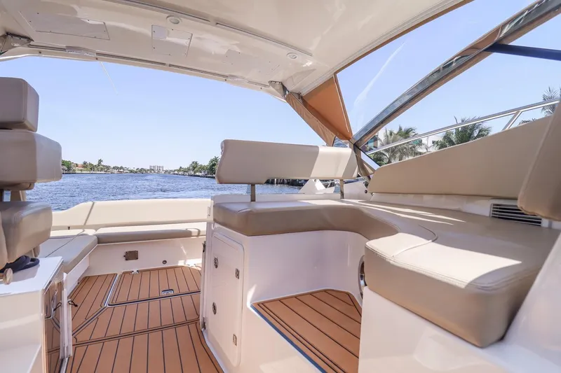 Slide: The Image of 2016 Pursuit SC 365i boat interior with beige seating and wooden flooring, overlooking a serene water view. - 17