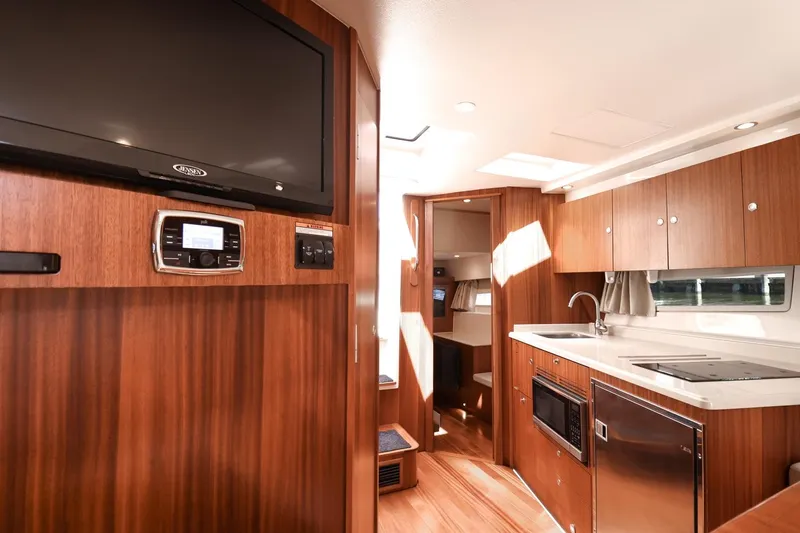 Slide: The Image of 2016 Pursuit SC 365i yacht interior with modern kitchen, wood cabinetry, and entertainment system. - 24
