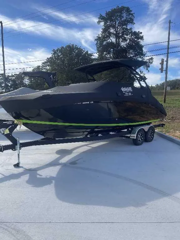 Slide: The Image of 2021 Yamaha Boats 255X on trailer, black with green stripe, parked outdoors. - 17