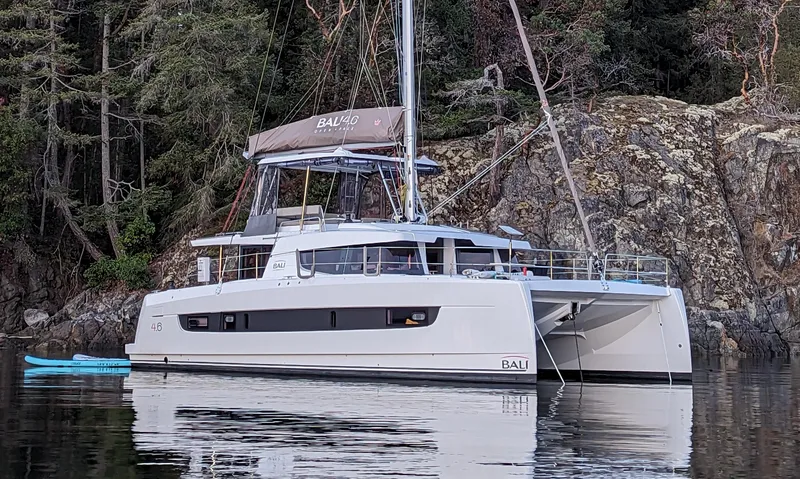 The Image of 2022 Bali 4.6 catamaran anchored near rocky shoreline with lush trees. - 0