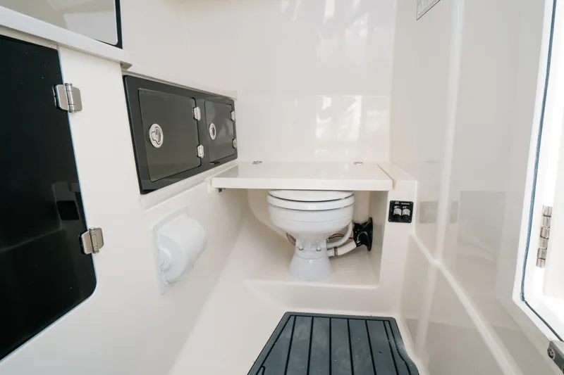 Slide: The Image of 2024 Cobia 330 Dual Console boat interior with compact marine toilet and storage cabinets. - 14