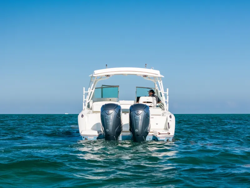 Slide: The Image of 2024 Cobia 330 Dual Console boat on open water, rear view with twin engines. - 19