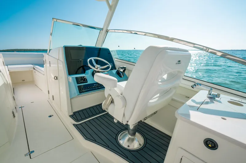 Slide: The Image of 2024 Cobia 330 Dual Console boat interior with helm, steering wheel, and ocean view. - 2