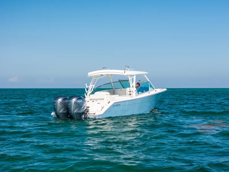 Slide: The Image of 2024 Cobia 330 Dual Console boat on open sea, featuring twin outboard engines. - 22