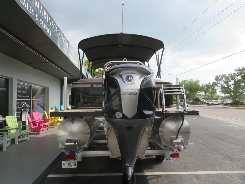 Slide: The Image of 2025 Avalon LSZ Quad Lounger pontoon boat with outboard motor, parked at a marine dealership. - 6