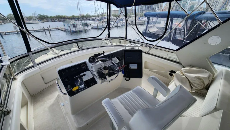 Slide: The Image of 1995 Carver 440 Aft Cabin Motor Yacht helm with marina view, featuring steering wheel and controls. - 13