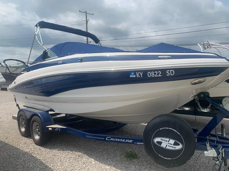 Slide: The Image of 2012 Crownline E1EC1Z boat on trailer, blue and white, parked outdoors. - 0