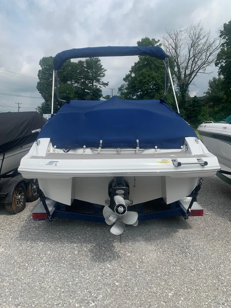 Slide: The Image of 2012 Crownline E1EC1Z boat with blue cover, parked on gravel. - 1