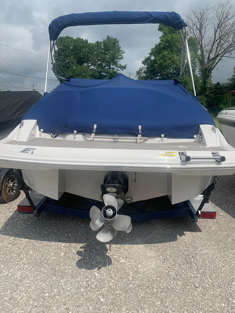 Slide: The Image of 2012 Crownline E1EC1Z boat with blue cover, rear view, parked on gravel. - 4