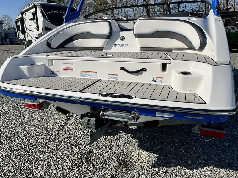 Slide: The Image of 2021 Yamaha AR195 boat rear view, showcasing swim platform and seating on gravel surface. - 6