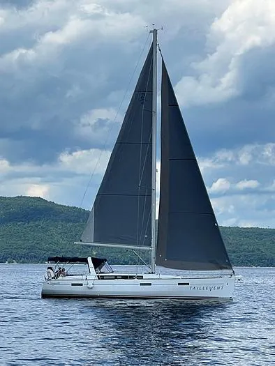Slide: The Image of 2018 Beneteau 45 sailboat with dark sails on a calm lake under cloudy skies. - 0