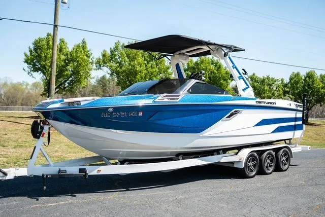 Slide: The Image of 2022 Centurion Ri265 boat on trailer, blue and white design, parked outdoors. - 0
