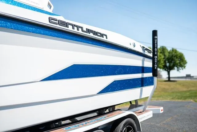 Slide: The Image of 2022 Centurion Ri265 boat with blue accents on a trailer, parked outdoors. - 2