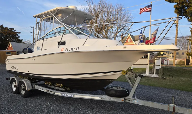 Slide: The Image of 2004 Robalo R235 Walkaround boat on trailer, parked outdoors with flags in background. - 12