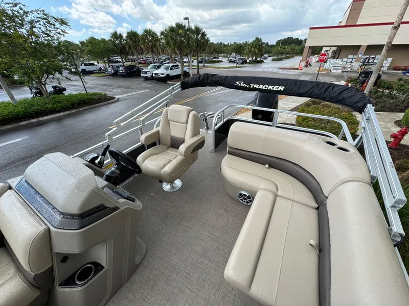 Slide: The Image of 2025 Sun Tracker Party Barge 18 DLX pontoon boat with seating and steering console, parked outdoors. - 3