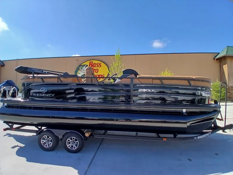 Slide: The Image of 2025 Regency 230 LE3 pontoon boat on trailer outside Bass Pro Shops. - 2