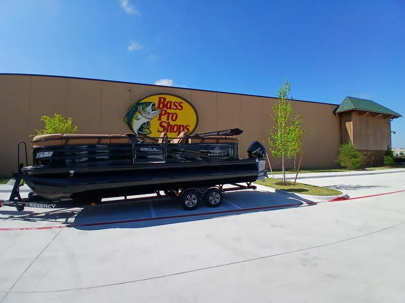 Slide: The Image of 2025 Regency 230 LE3 boat on trailer outside Bass Pro Shops under clear blue sky. - 5