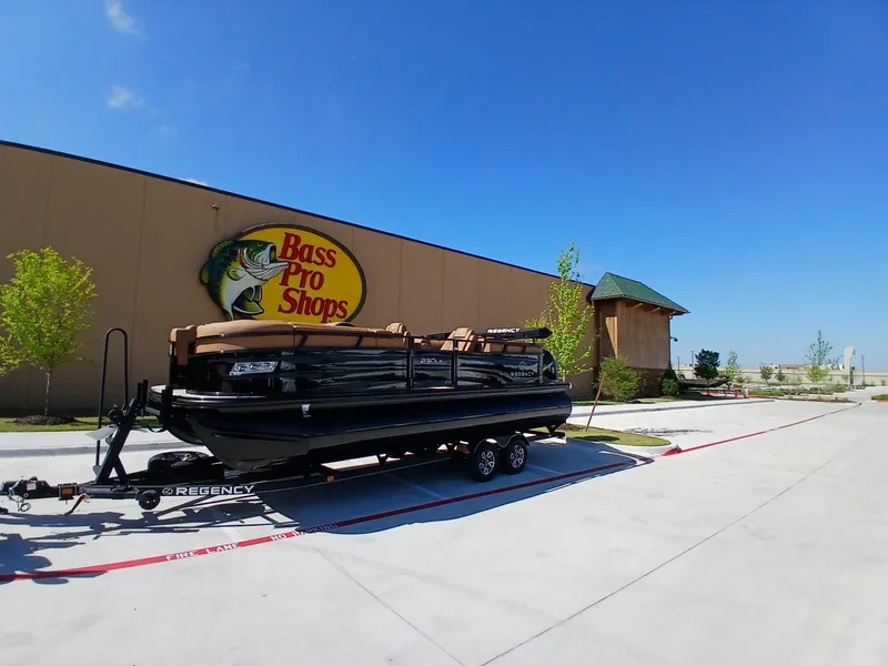 Slide: The Image of 2025 Regency 230 LE3 boat on trailer outside Bass Pro Shops under clear blue sky. - 6