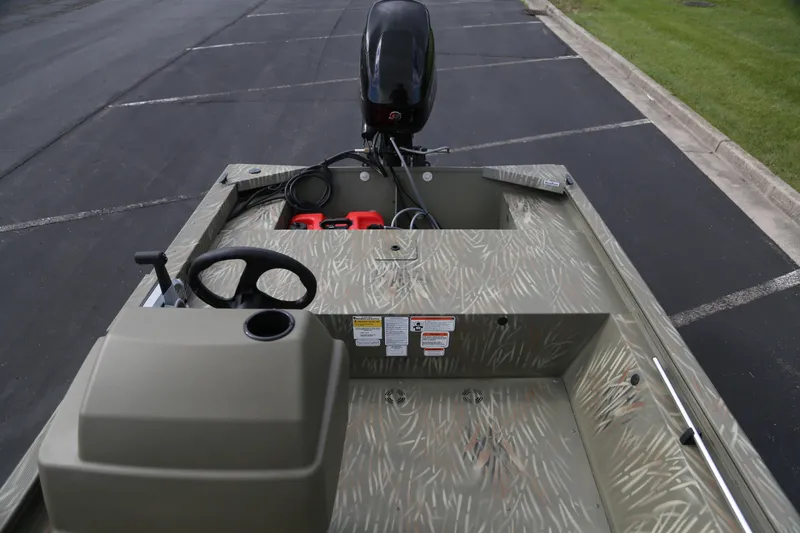 Slide: The Image of 2025 Tracker Grizzly 1648 SC boat interior with steering wheel and motor, parked on pavement. - 3