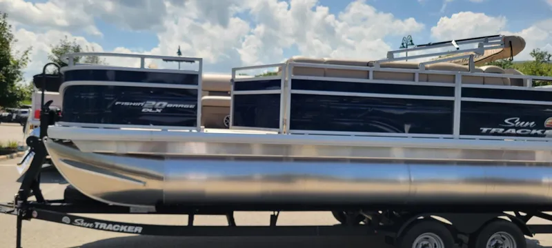Slide: The Image of 2025 Sun Tracker Fishin' Barge 20 DLX pontoon boat on trailer under a cloudy sky. - 2