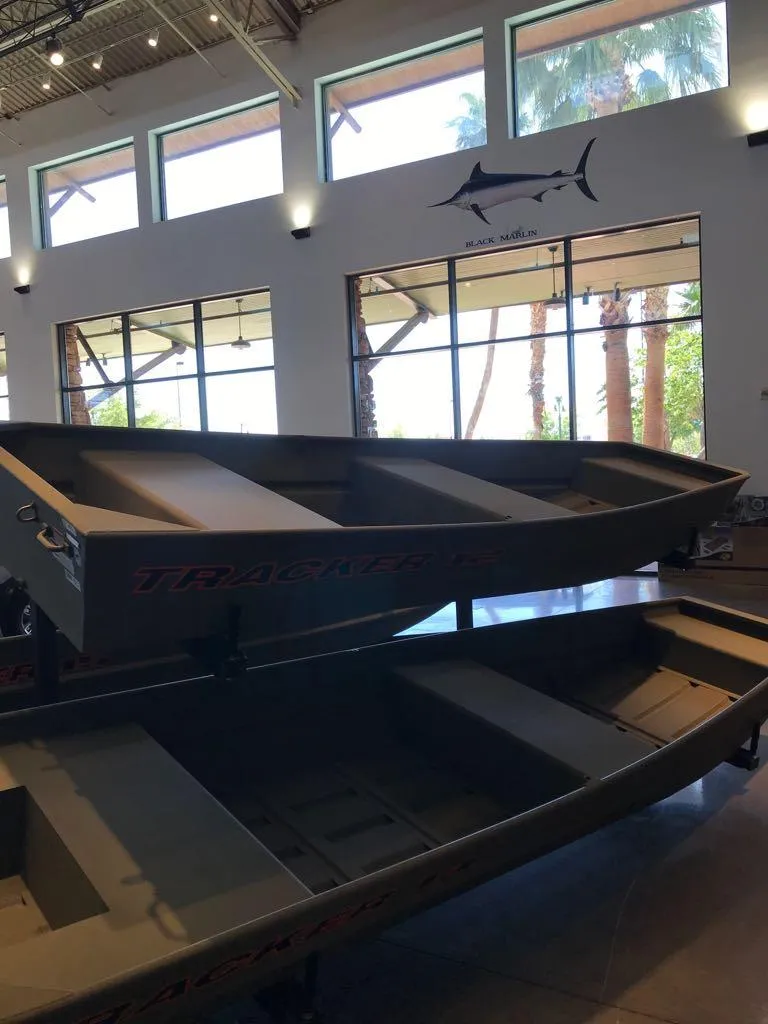 Slide: The Image of 2025 Tracker Grizzly 12 Jon boat displayed indoors with large windows and palm trees outside. - 3