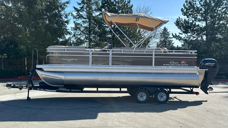 Slide: The Image of 2025 Sun Tracker SportFish 22 XP3 pontoon boat on trailer, parked outdoors. - 2