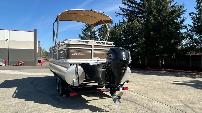 Slide: The Image of 2025 Sun Tracker SportFish 22 XP3 pontoon boat with canopy and outboard motor in a parking lot. - 3