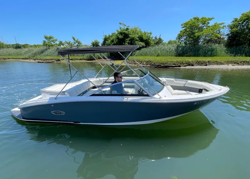 Slide: The Image of 2018 Cobalt CS22 boat on calm water, sunny day, lush greenery in background. - 2