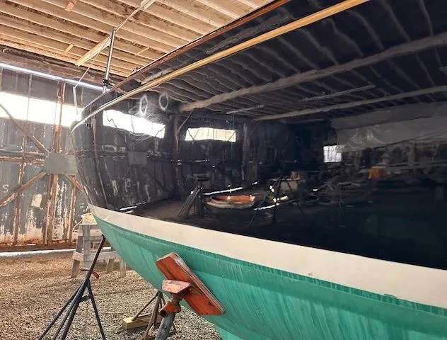Slide: The Image of 1972 Bristol 40 sailboat in a workshop, hull partially painted, supported by stands. - 4