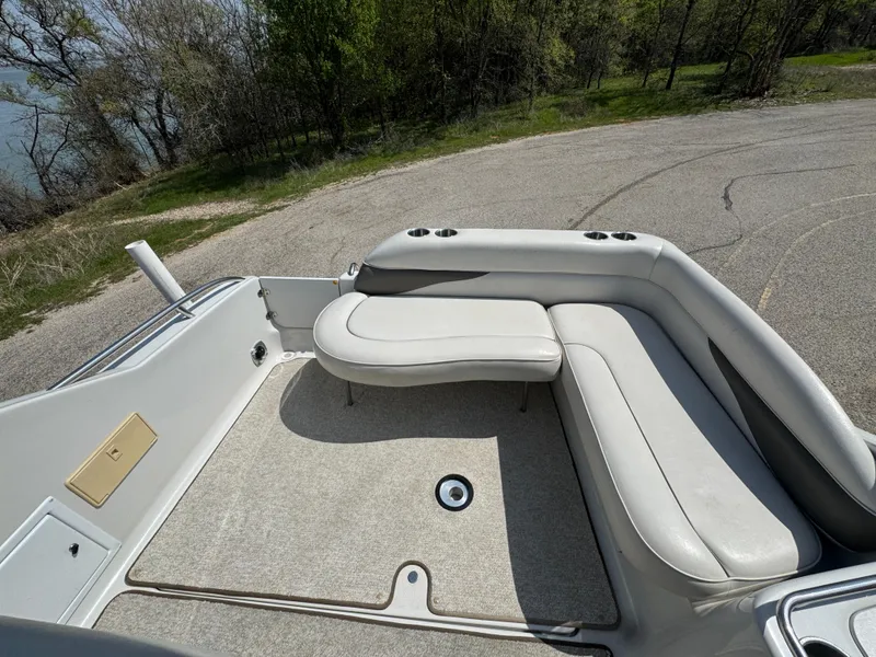 Slide: The Image of 2003 Crownline 262 CR boat interior with cushioned seating and cup holders, parked near a lake. - 11
