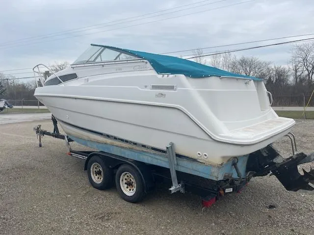 Slide: The Image of 1997 Bayliner 2355 SJ Ciera boat on trailer, white hull, teal cover, parked outdoors. - 2