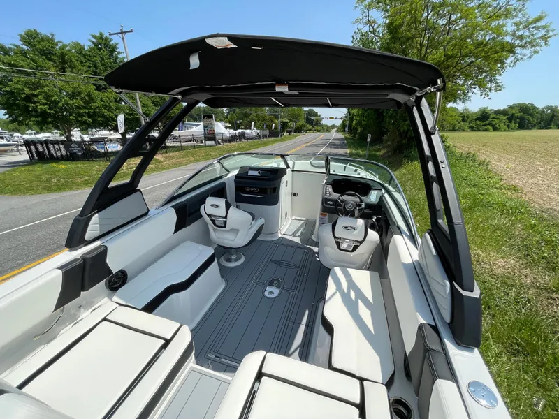 Slide: The Image of 2024 Chaparral 250 OSX boat interior with seating, steering wheel, and canopy on a sunny day. - 49