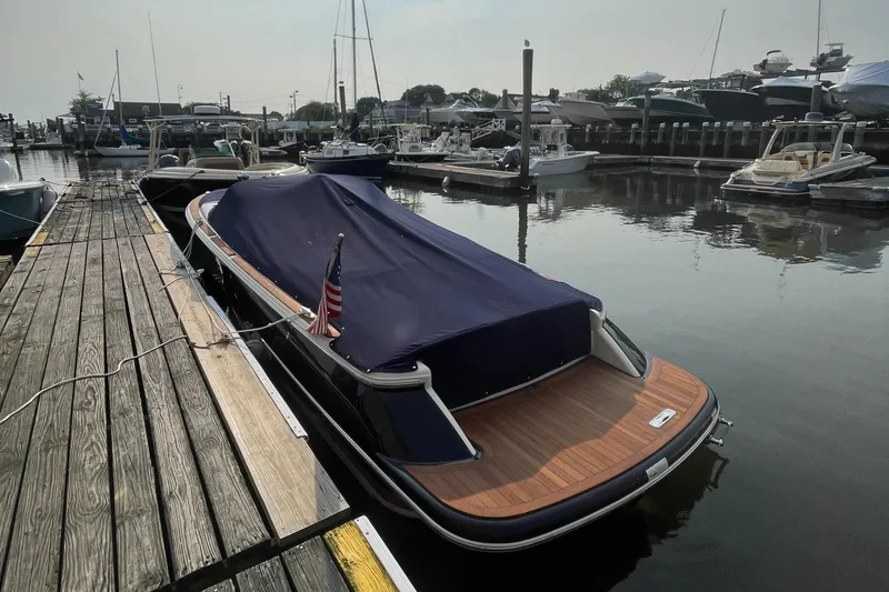 Slide: The Image of 2016 Chris-Craft Launch 25 boat docked with cover, wooden deck, and American flag. - 40