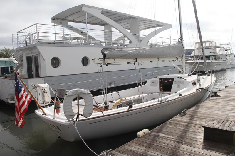 Slide: The Image of 2009 e Sailing Yachts e33 docked beside a large houseboat, displaying an American flag. - 5