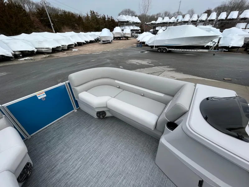 Slide: The Image of 2025 Godfrey Xperience Cruise boat interior with gray seating, parked among covered boats. - 8