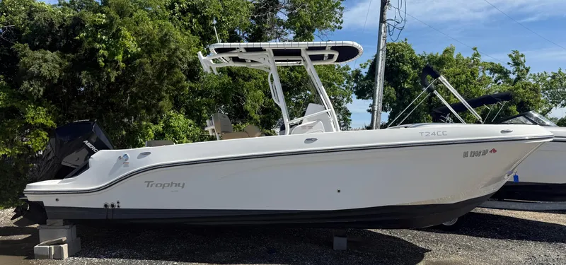 Slide: The Image of 2022 Trophy T24CC boat, white hull, parked outdoors, surrounded by trees. - 1