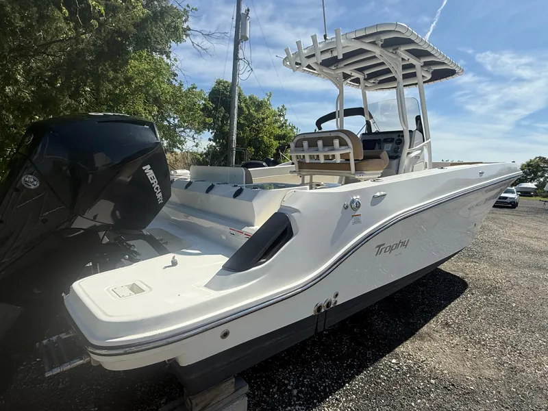 Slide: The Image of 2022 Trophy T24CC boat with Mercury engine, parked outdoors on gravel. - 2