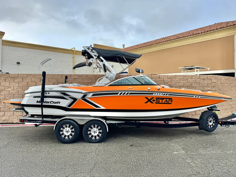 Slide: The Image of 2015 MasterCraft XStar boat in vibrant orange on a trailer, parked outdoors. - 0