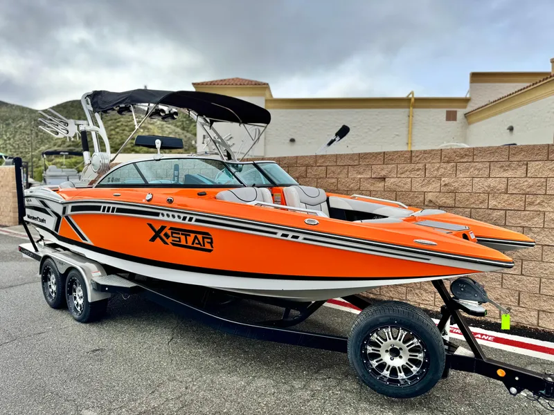 Slide: The Image of 2015 MasterCraft XStar boat in vibrant orange on a trailer, parked outdoors. - 1