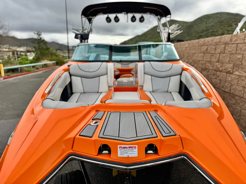 Slide: The Image of 2015 MasterCraft XStar boat with orange exterior and gray seating, parked outdoors. - 13