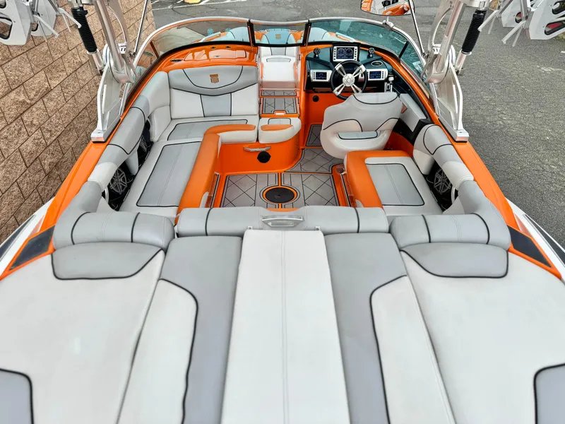 Slide: The Image of 2015 MasterCraft XStar boat interior with orange and gray seating, modern dashboard, and spacious layout. - 14
