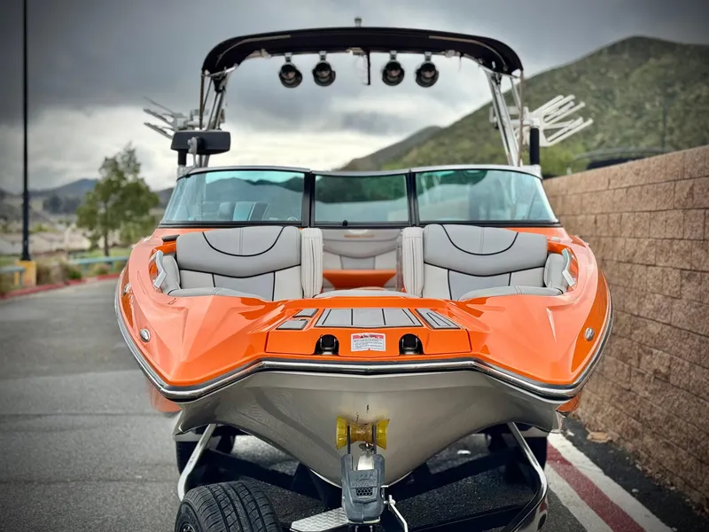 Slide: The Image of 2015 MasterCraft XStar boat with orange exterior, parked on a trailer, mountainous background. - 2