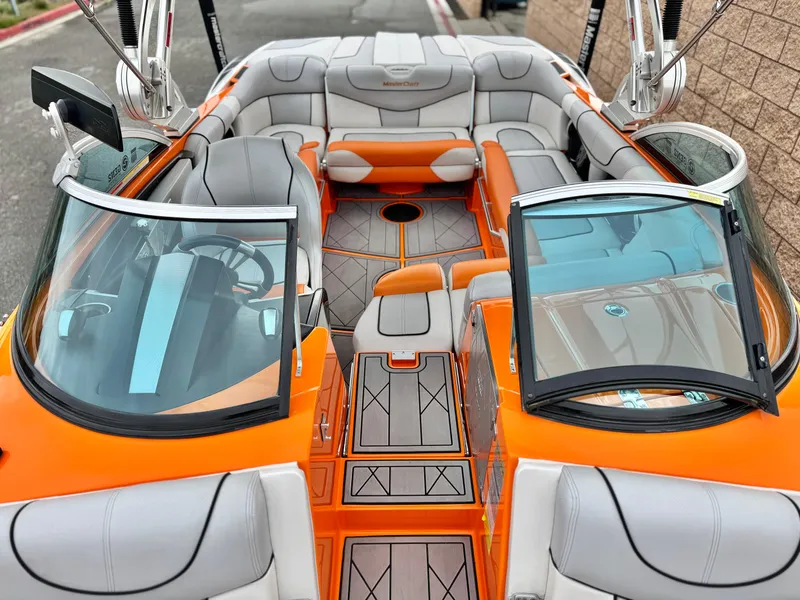 Slide: The Image of 2015 MasterCraft XStar boat interior with orange and gray seating, open windshield, and modern design. - 26