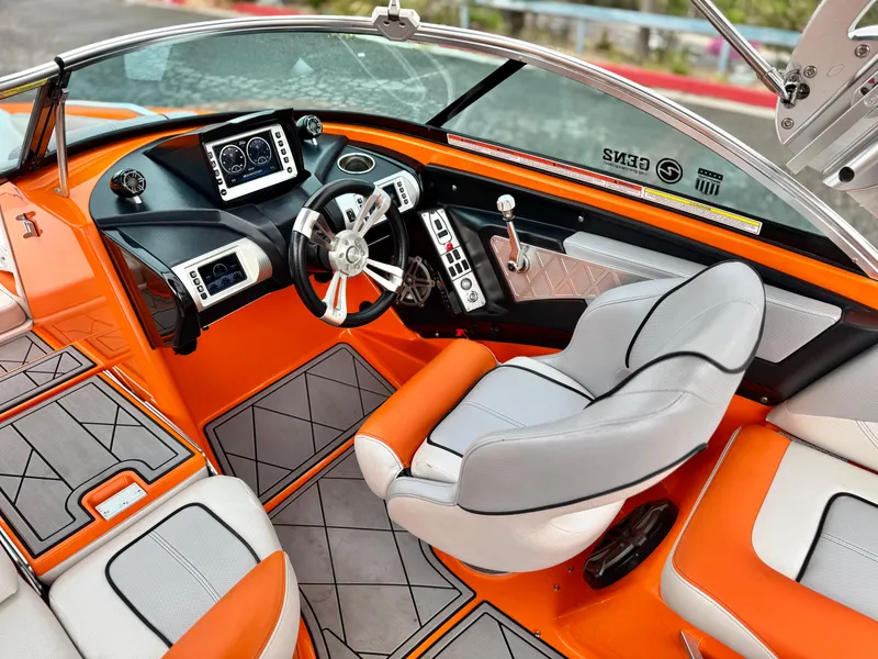 Slide: The Image of 2015 MasterCraft XStar boat interior with orange and gray seating, modern dashboard, and steering wheel. - 43