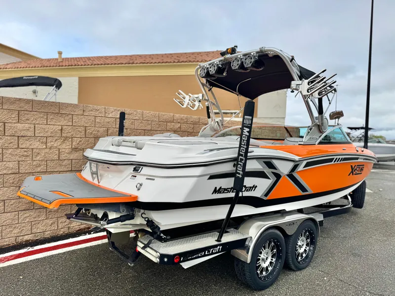 Slide: The Image of 2015 MasterCraft XStar boat on trailer, featuring orange and white design, parked outdoors. - 5