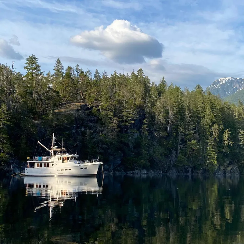 Slide: The Image of Selene 47 yacht from 2003 on calm water, surrounded by lush forest and mountains. - 9