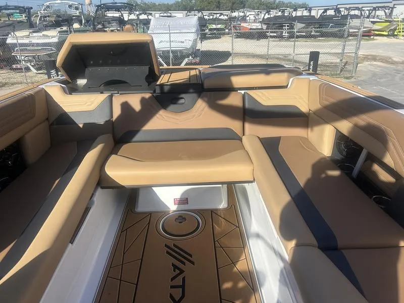 Slide: The Image of 2025 ATX Surf Boats 24 Type-S interior with tan seating and deck, parked outdoors. - 3