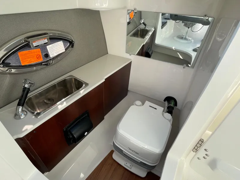 Slide: The Image of 2025 Chaparral 267 SSX boat bathroom with sink, mirror, and portable toilet. - 29